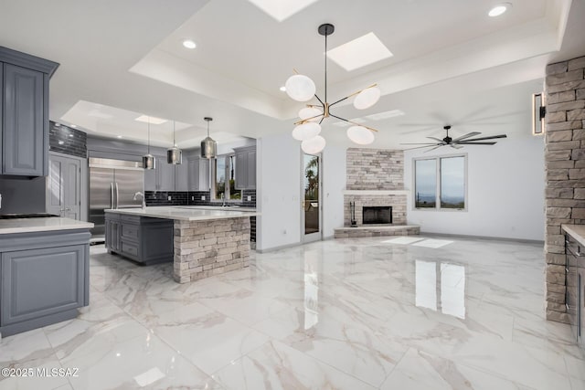 kitchen featuring built in refrigerator, gray cabinetry, hanging light fixtures, a kitchen island, and a raised ceiling