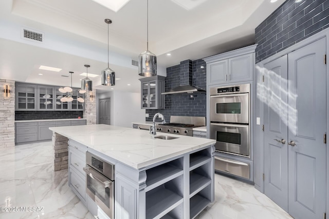 kitchen featuring a kitchen island with sink, hanging light fixtures, gray cabinets, and stainless steel double oven