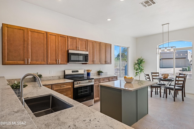 kitchen featuring decorative light fixtures, sink, a center island, stainless steel appliances, and light stone countertops