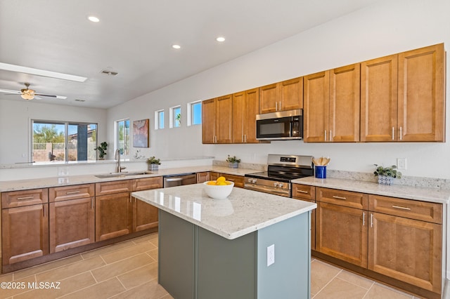 kitchen with sink, a center island, light tile patterned floors, appliances with stainless steel finishes, and light stone countertops