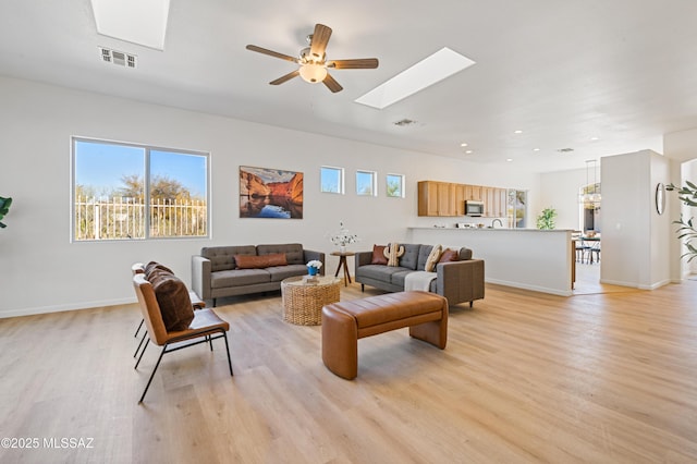 living room with a skylight, ceiling fan, and light wood-type flooring