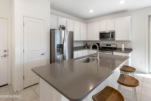 kitchen featuring a breakfast bar, white cabinets, appliances with stainless steel finishes, an island with sink, and dark countertops