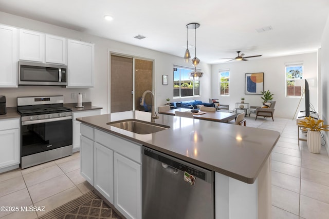 kitchen featuring stainless steel appliances, dark countertops, a sink, and a kitchen island with sink