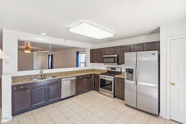 kitchen with sink, appliances with stainless steel finishes, dark brown cabinets, light stone counters, and kitchen peninsula