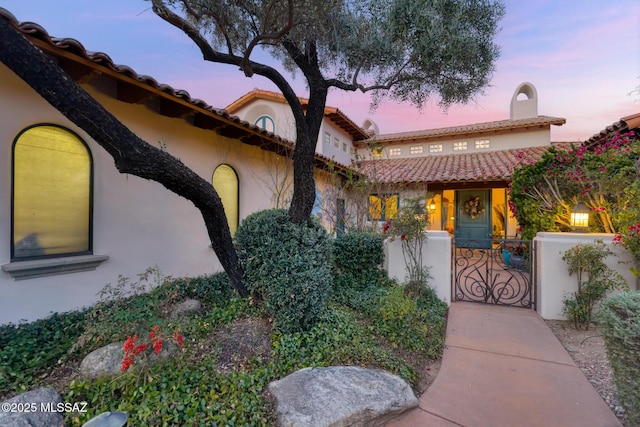 mediterranean / spanish-style house with a fenced front yard, a gate, a tiled roof, and stucco siding