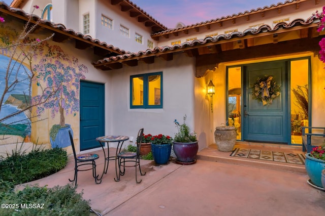 exterior entry at dusk featuring a garage, a patio area, and stucco siding