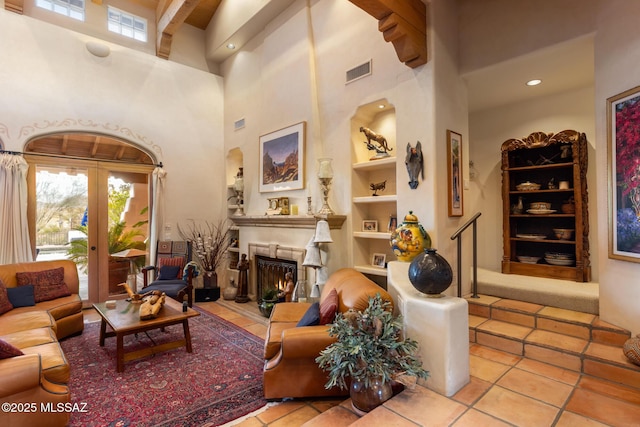 living room with a warm lit fireplace, french doors, built in shelves, and visible vents