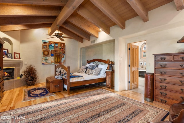 bedroom featuring lofted ceiling with beams, a tiled fireplace, wood finished floors, and visible vents