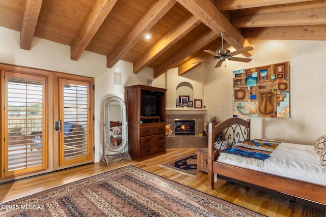 bedroom featuring access to exterior, vaulted ceiling with beams, wood-type flooring, a tiled fireplace, and wood ceiling