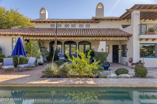 back of house with a chimney, an outdoor pool, a patio, and a balcony