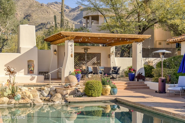 exterior space with an outdoor pool, a patio, a fireplace, a mountain view, and stucco siding