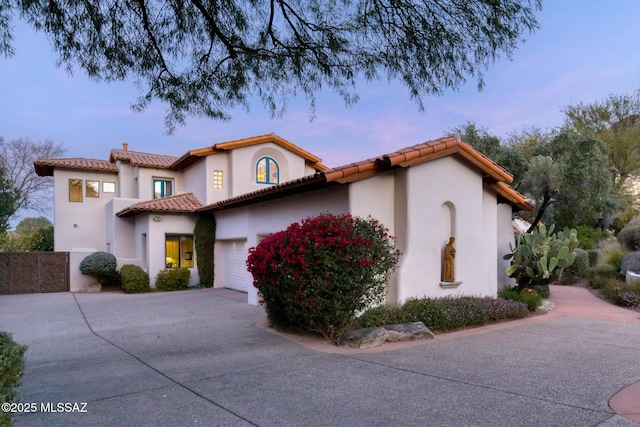 mediterranean / spanish-style house with a garage, a tiled roof, concrete driveway, and stucco siding