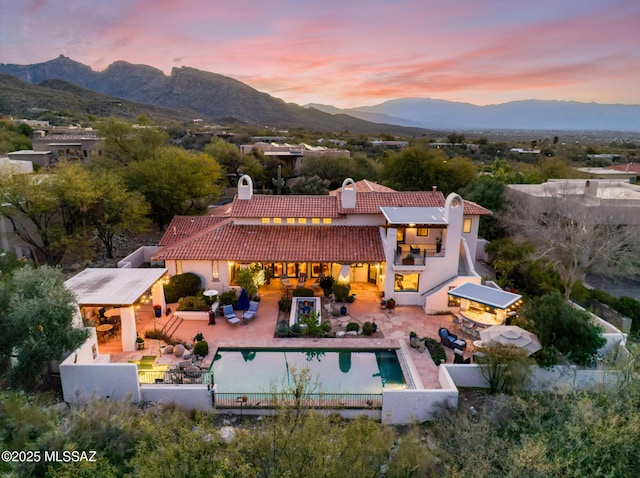 back of property at dusk with outdoor dry bar, a tiled roof, a fenced backyard, and a mountain view