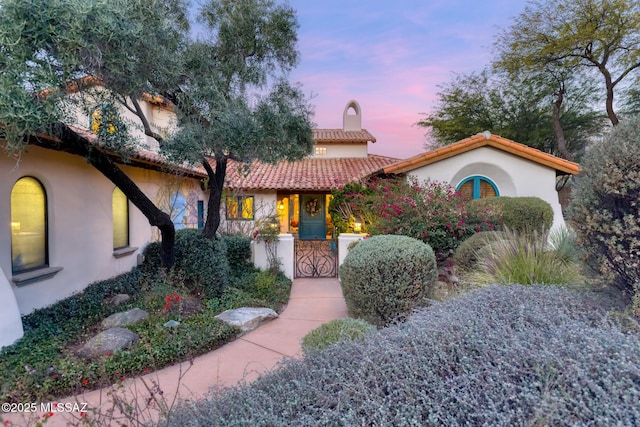 mediterranean / spanish-style house with a tile roof, a chimney, and stucco siding