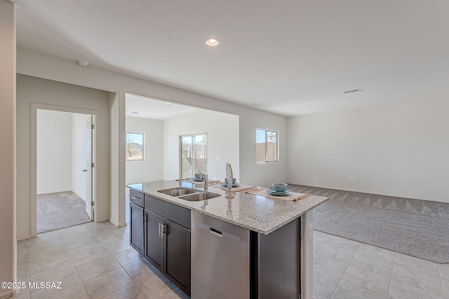 kitchen with sink, a kitchen island with sink, stainless steel dishwasher, light stone counters, and light carpet