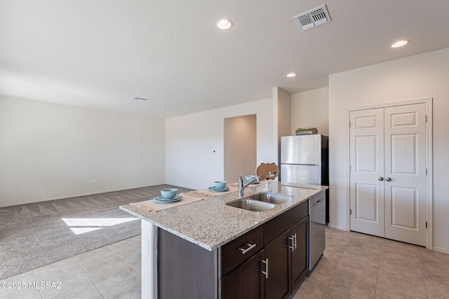 kitchen with sink, appliances with stainless steel finishes, dark brown cabinets, a center island with sink, and light colored carpet