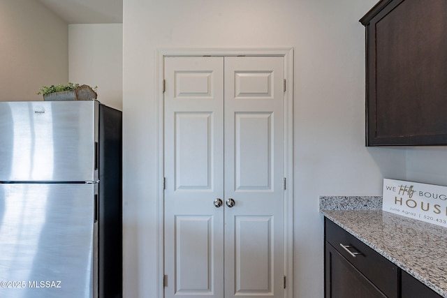 kitchen with dark brown cabinets, stainless steel fridge, and light stone counters