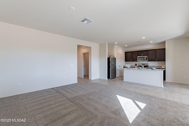 unfurnished living room featuring dark brown cabinetry, a kitchen island with sink, and light carpet