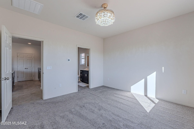 unfurnished bedroom featuring light colored carpet, ensuite bath, and a notable chandelier