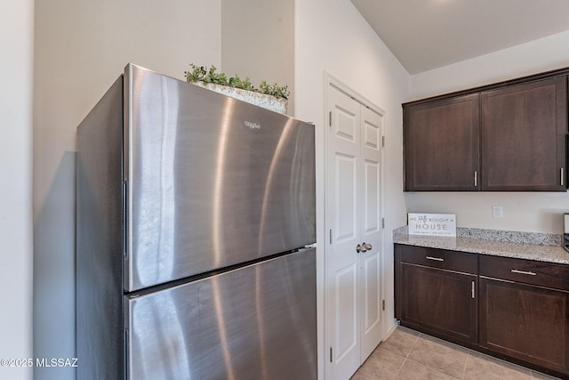 kitchen featuring light stone counters, stainless steel fridge, dark brown cabinets, and light tile patterned floors