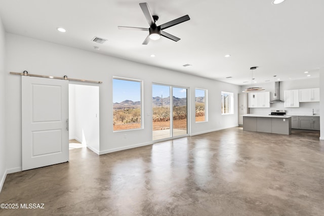 unfurnished living room with sink, concrete floors, ceiling fan, and a barn door