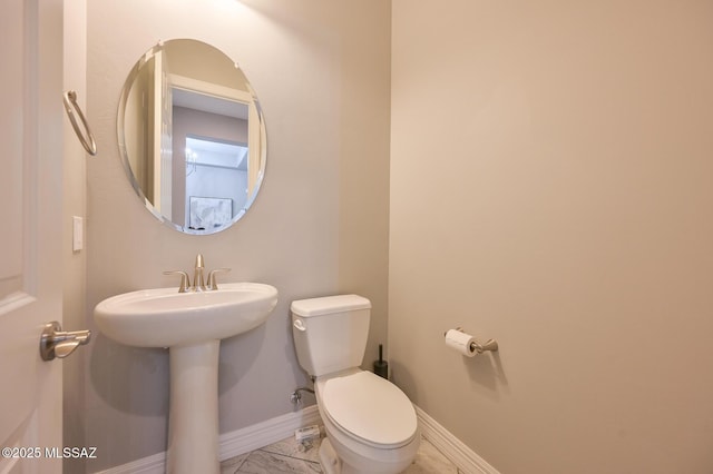 half bath with toilet, a sink, and baseboards