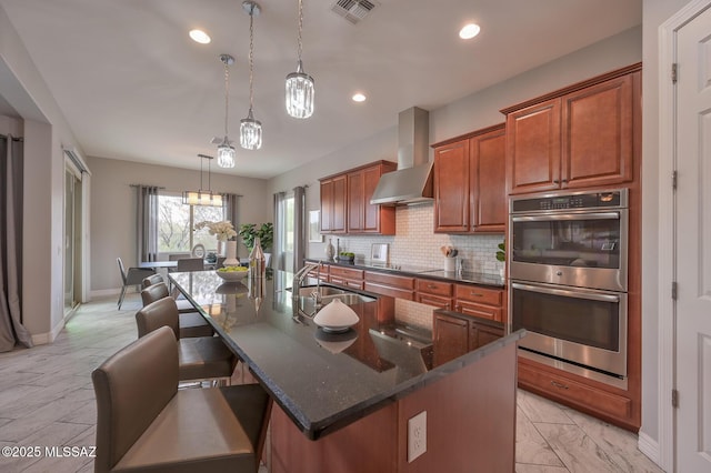 kitchen with double oven, wall chimney range hood, visible vents, a sink, and backsplash