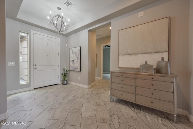 foyer with a tray ceiling, a chandelier, baseboards, and visible vents