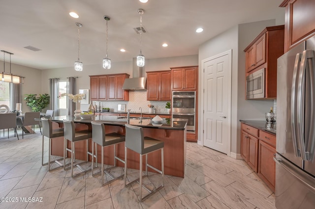 kitchen with wall chimney range hood, visible vents, brown cabinets, decorative backsplash, and appliances with stainless steel finishes