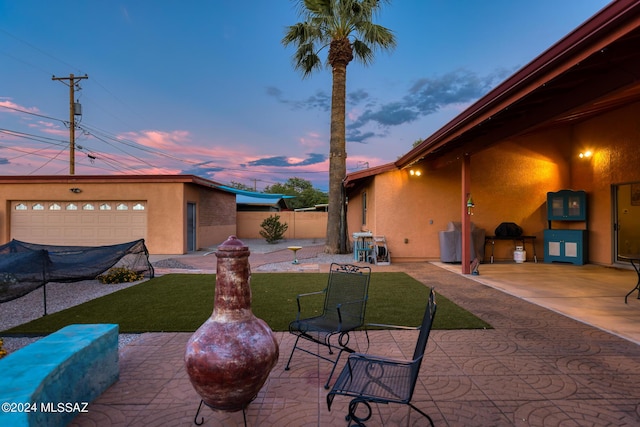 patio terrace at dusk with a garage and a yard