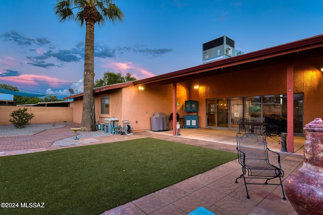 back house at dusk featuring a patio, central AC, and a lawn