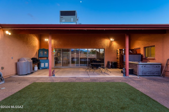 back house at dusk featuring a yard, central AC, and a patio area