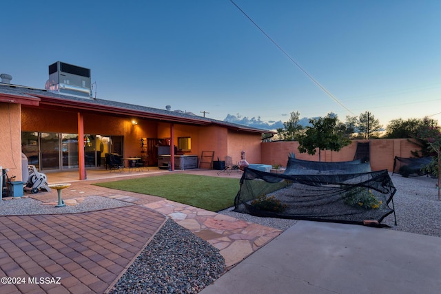 back house at dusk featuring a yard, central AC, a patio, and an outdoor kitchen