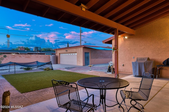 patio terrace at dusk with a grill, a garage, an outdoor structure, and a lawn