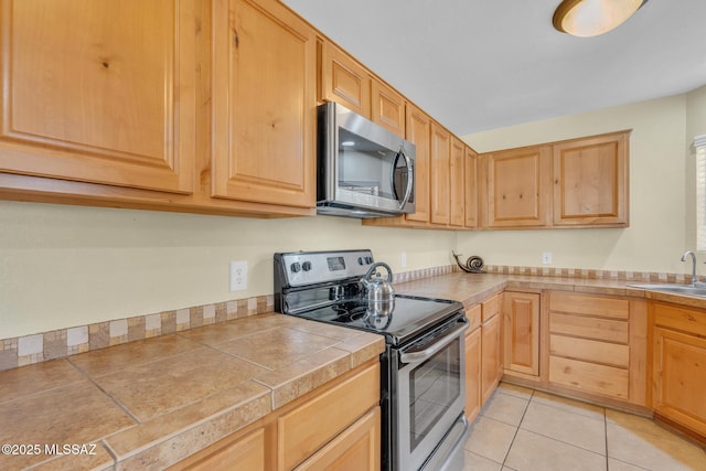 kitchen with stainless steel appliances, sink, light tile patterned floors, and light brown cabinetry