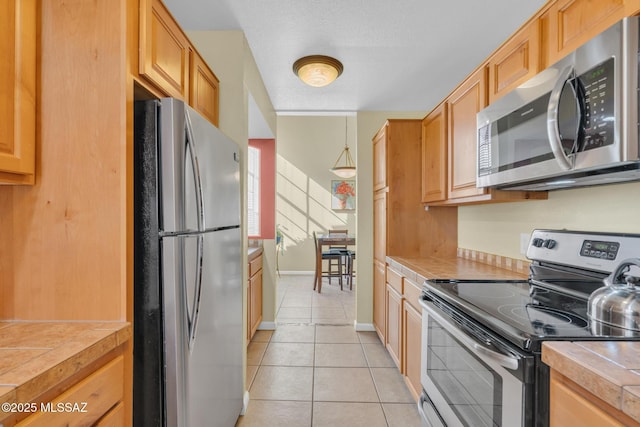 kitchen with light tile patterned floors, tile counters, stainless steel appliances, and a textured ceiling