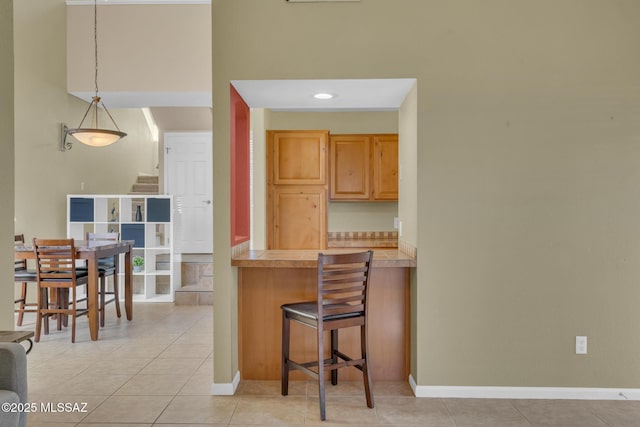 kitchen with light brown cabinets, a kitchen bar, hanging light fixtures, and light tile patterned floors