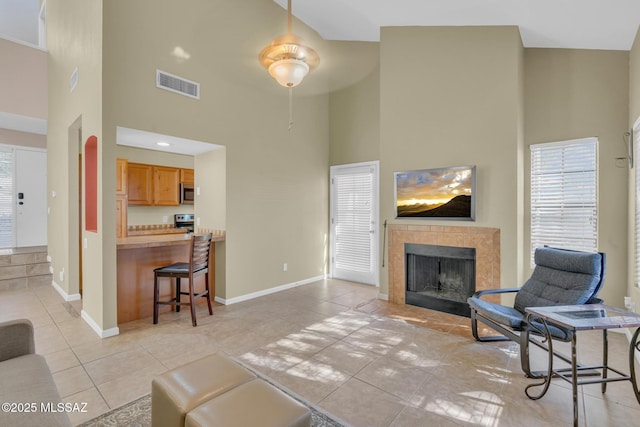 living room featuring a tiled fireplace, light tile patterned flooring, and a towering ceiling