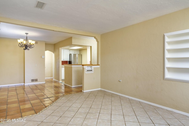 tiled empty room featuring a textured ceiling, an inviting chandelier, and built in shelves