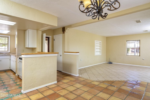 kitchen with an inviting chandelier, light tile patterned floors, kitchen peninsula, and white cabinets