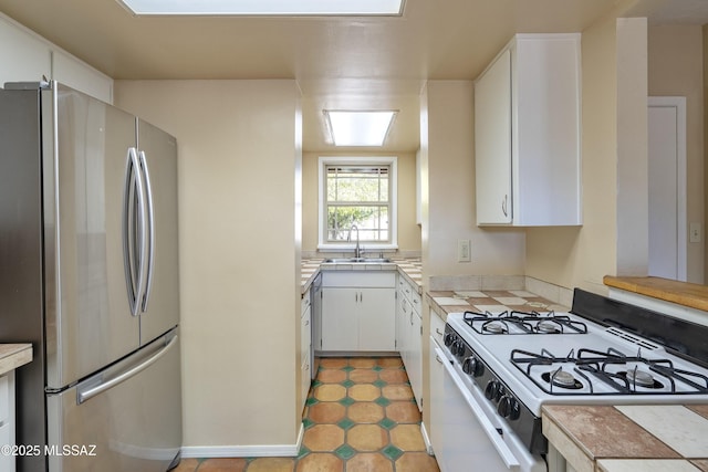 kitchen with tile countertops, stainless steel refrigerator, white cabinetry, sink, and white range with gas cooktop