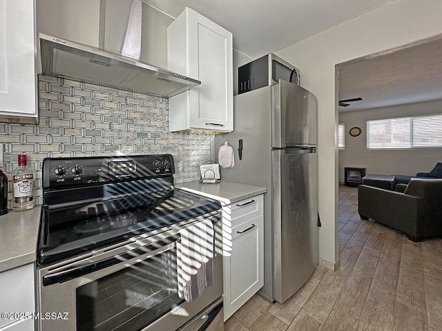 kitchen with wall chimney range hood, white cabinetry, stainless steel appliances, tasteful backsplash, and light wood-type flooring