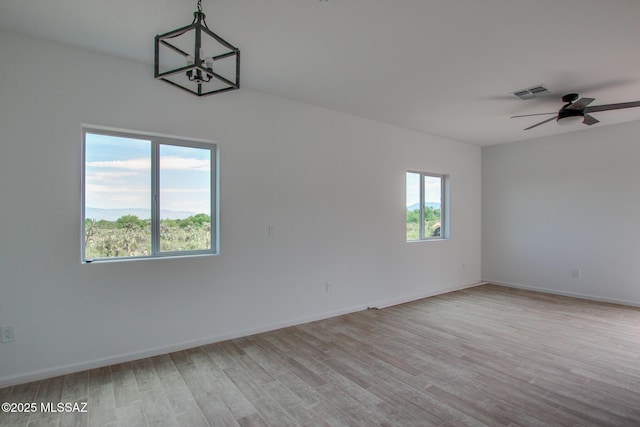 unfurnished room with ceiling fan with notable chandelier and light hardwood / wood-style floors