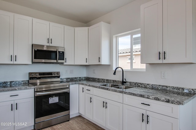 kitchen featuring white cabinetry, sink, dark stone countertops, stainless steel appliances, and light hardwood / wood-style flooring