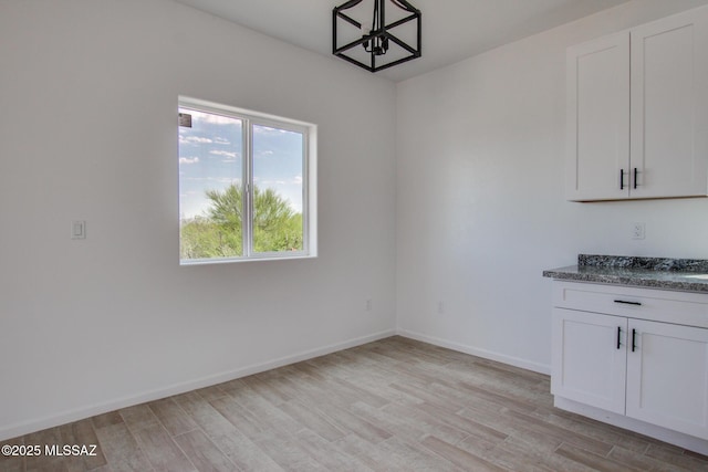 unfurnished dining area featuring an inviting chandelier and light hardwood / wood-style flooring