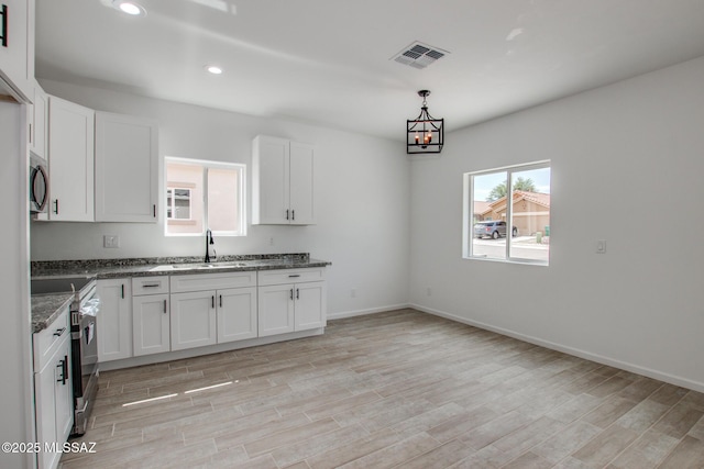 kitchen with sink, dark stone countertops, stainless steel appliances, white cabinets, and light wood-type flooring