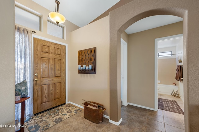 tiled entryway featuring arched walkways, lofted ceiling, and baseboards