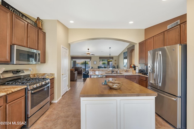 kitchen with arched walkways, a peninsula, a sink, open floor plan, and appliances with stainless steel finishes