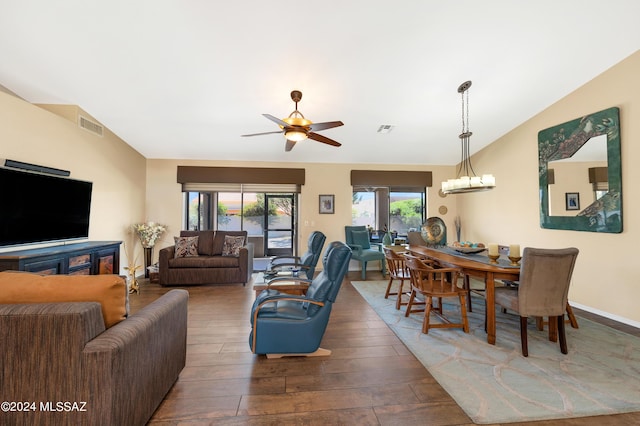 living area featuring vaulted ceiling, dark wood-style flooring, ceiling fan with notable chandelier, and visible vents