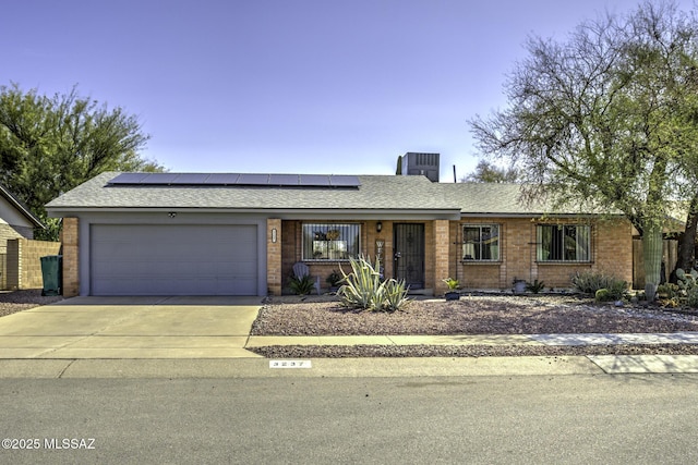 ranch-style home with brick siding, solar panels, a shingled roof, concrete driveway, and an attached garage